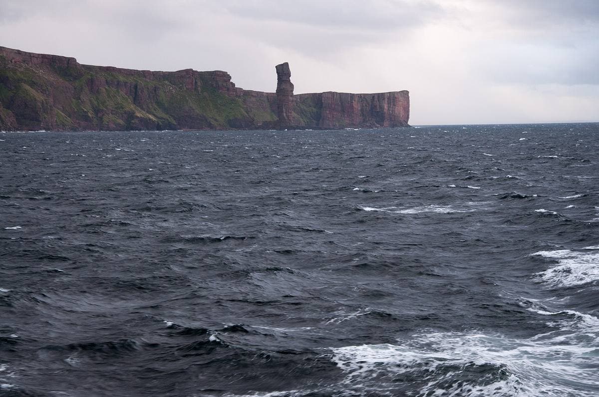 A tall red sandstone sea stack beside cliffs