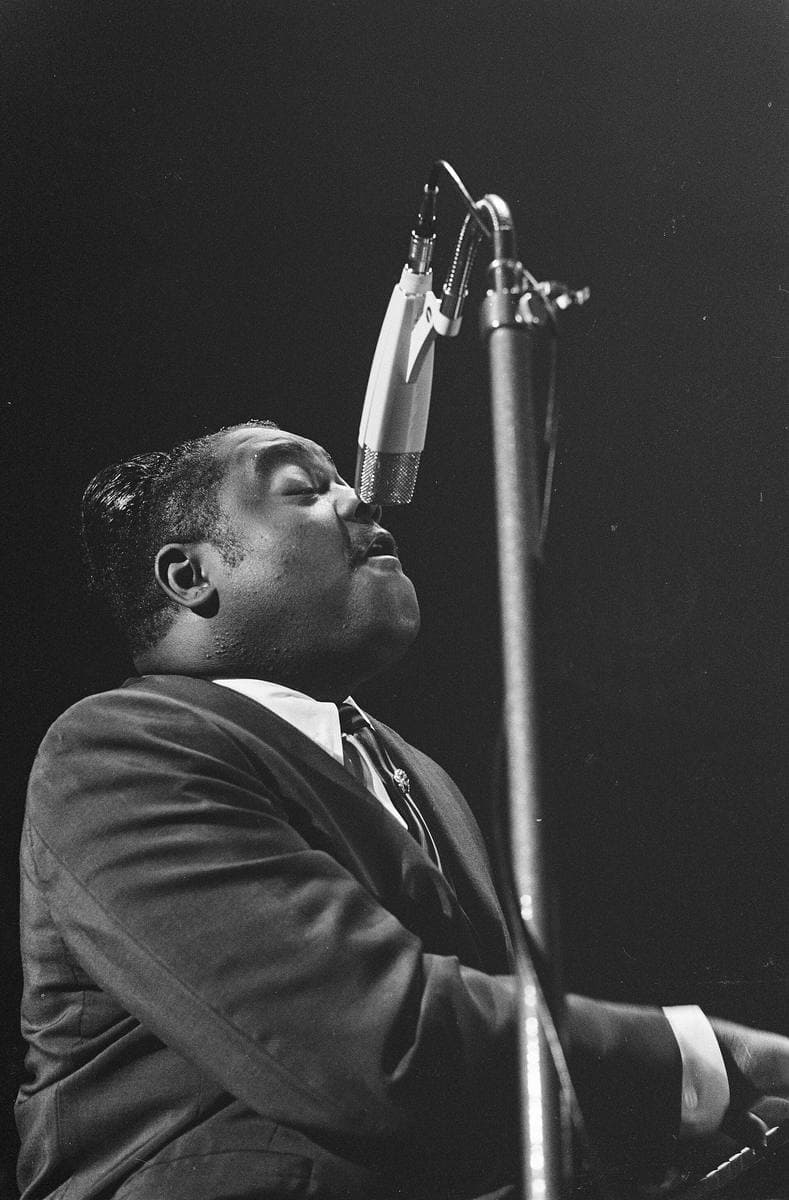 Fats Domino at the piano singing into a microphone, head tilted back