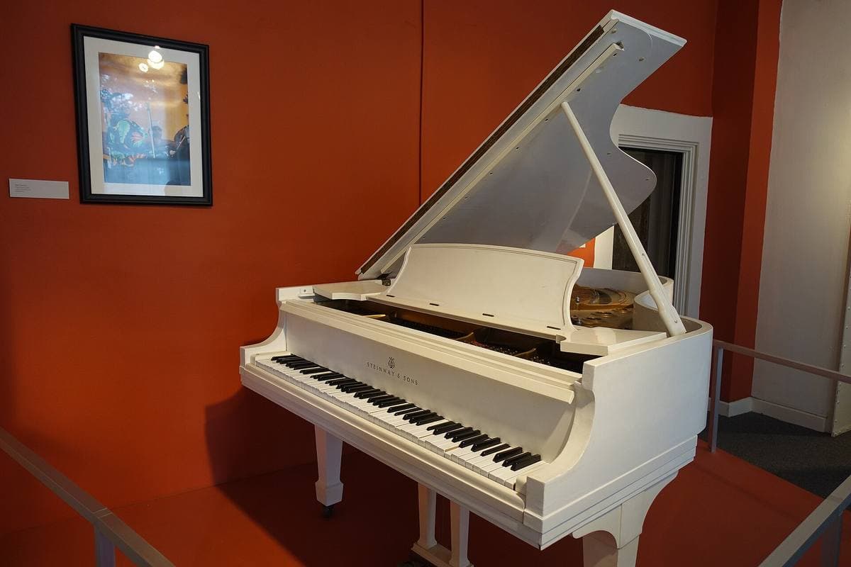 A white grand piano with its lid raised in a red museum room