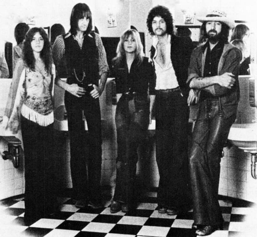 The five members of Fleetwood Mac in black and white, standing on a chequered floor in a tiled washroom
