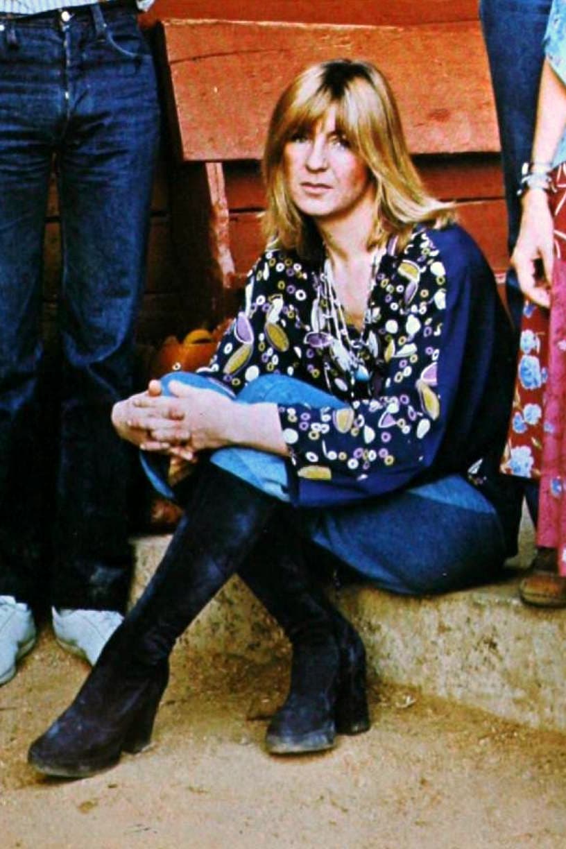 Christine McVie sitting on a low step in a patterned blouse and boots