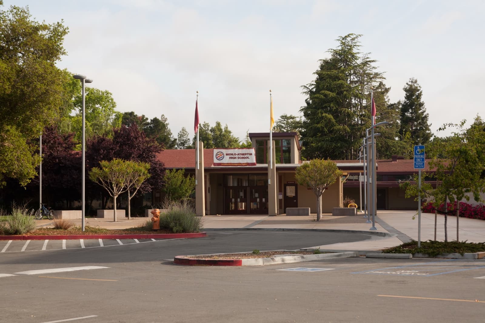 A low school entrance with a flagpole and trees beyond a drop-off loop