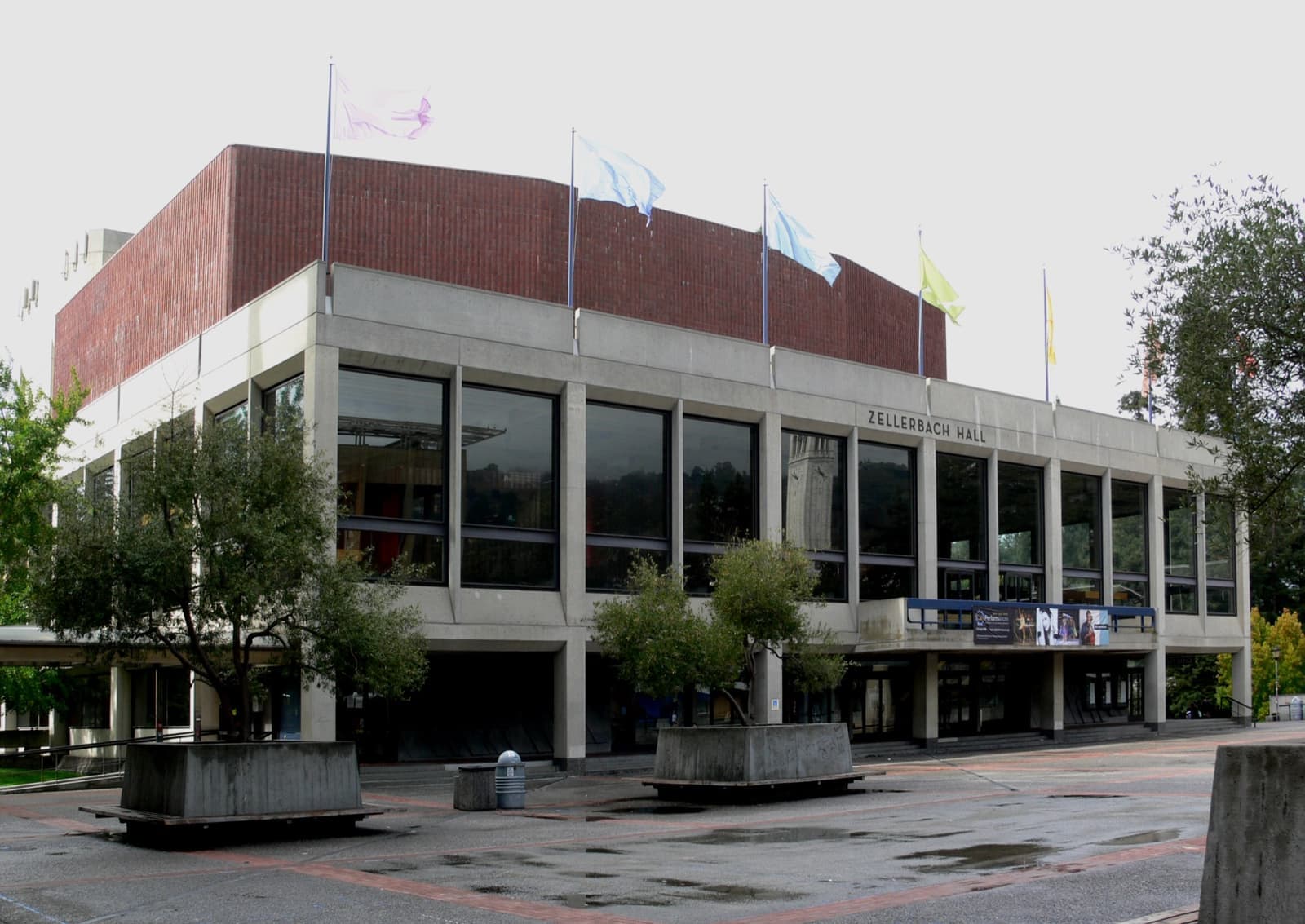 A long modernist concert hall with a glass front and brick upper storey across a plaza