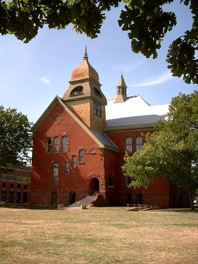 A small red-brick building with a bell tower among trees