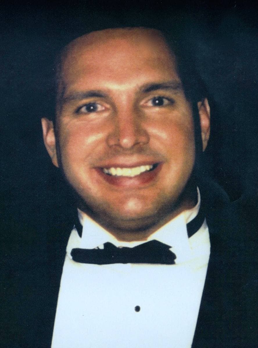 Garth Brooks in a tuxedo and bow tie, smiling broadly, against a dark background