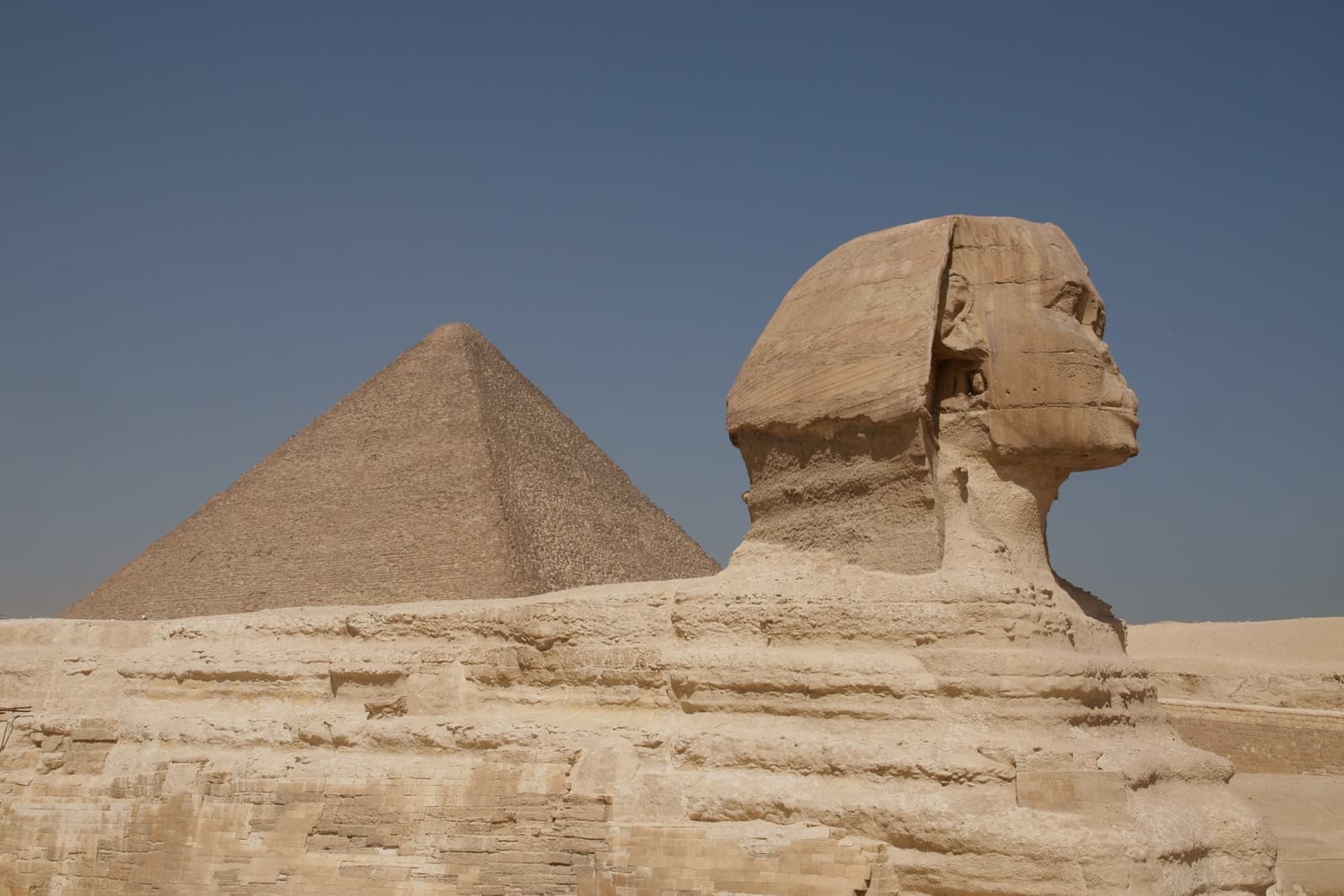 The Sphinx in profile in front of the Great Pyramid under a hazy sky