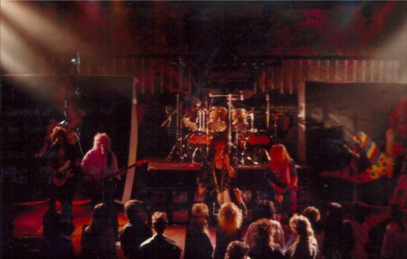 A rock band playing on a small stage to a crowd, lit by spotlights