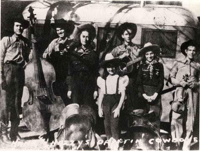 A small group of young men in hats with guitars and a fiddle, posed for a band photograph