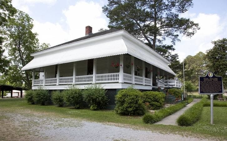 A small white wooden house with a porch, now a museum