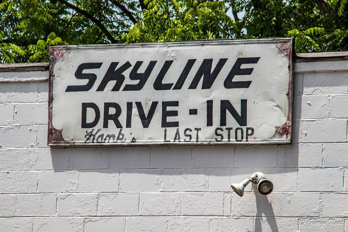 A small white roadside drive-in building with a hand-painted sign