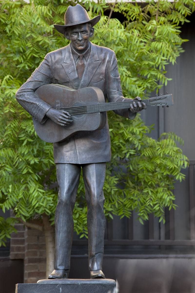 A bronze statue of Hank Williams in a hat holding a guitar