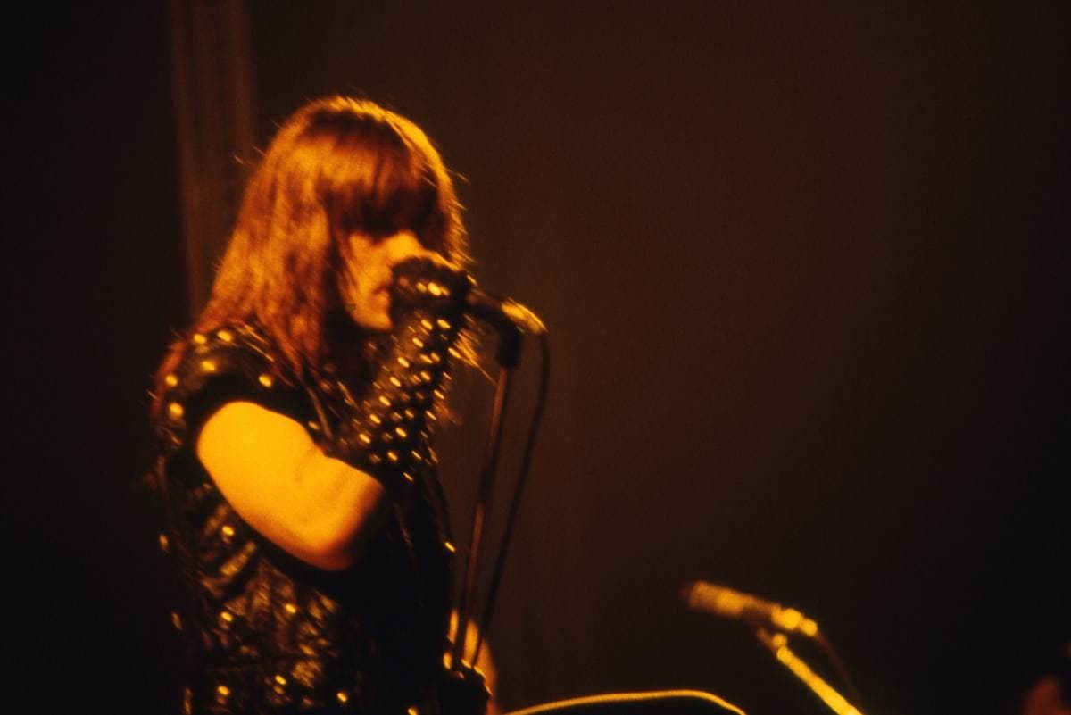A long-haired singer at a microphone in orange stage light