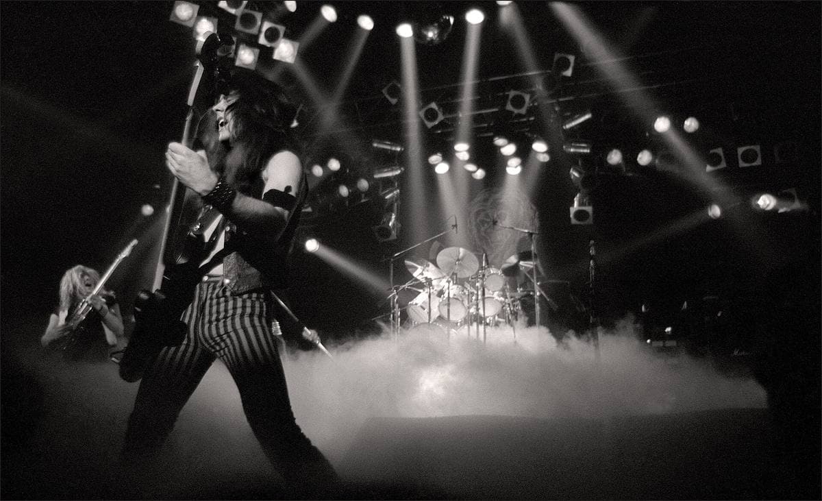 A bass player in front of a drum riser half hidden in low white fog