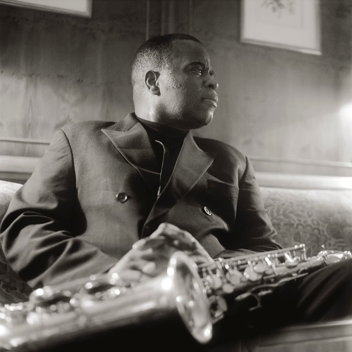 Maceo Parker seated in a suit, a saxophone across his lap
