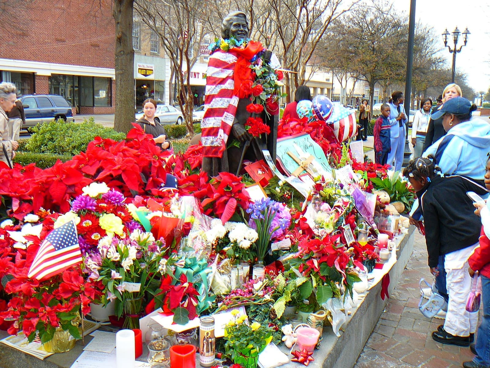The bronze statue draped in flags and garlands, surrounded by poinsettias, candles and people