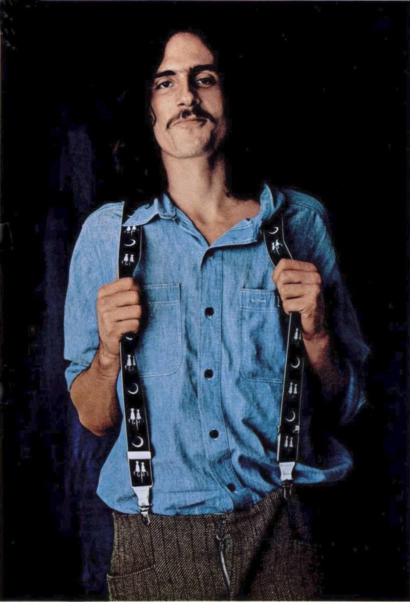 James Taylor with long hair and a moustache, looking at the camera