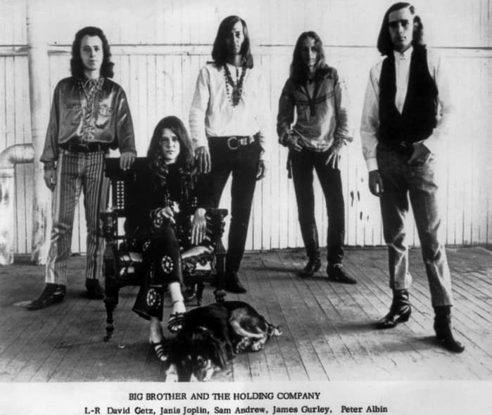Black-and-white group portrait of the five band members, Janis Joplin seated in the centre with a dog at her feet
