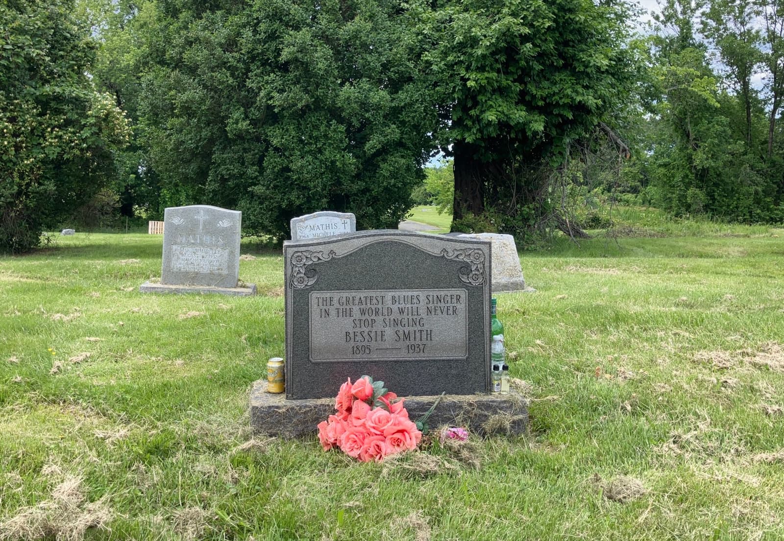 A grey granite headstone for Bessie Smith in a grassy cemetery, with flowers at its foot