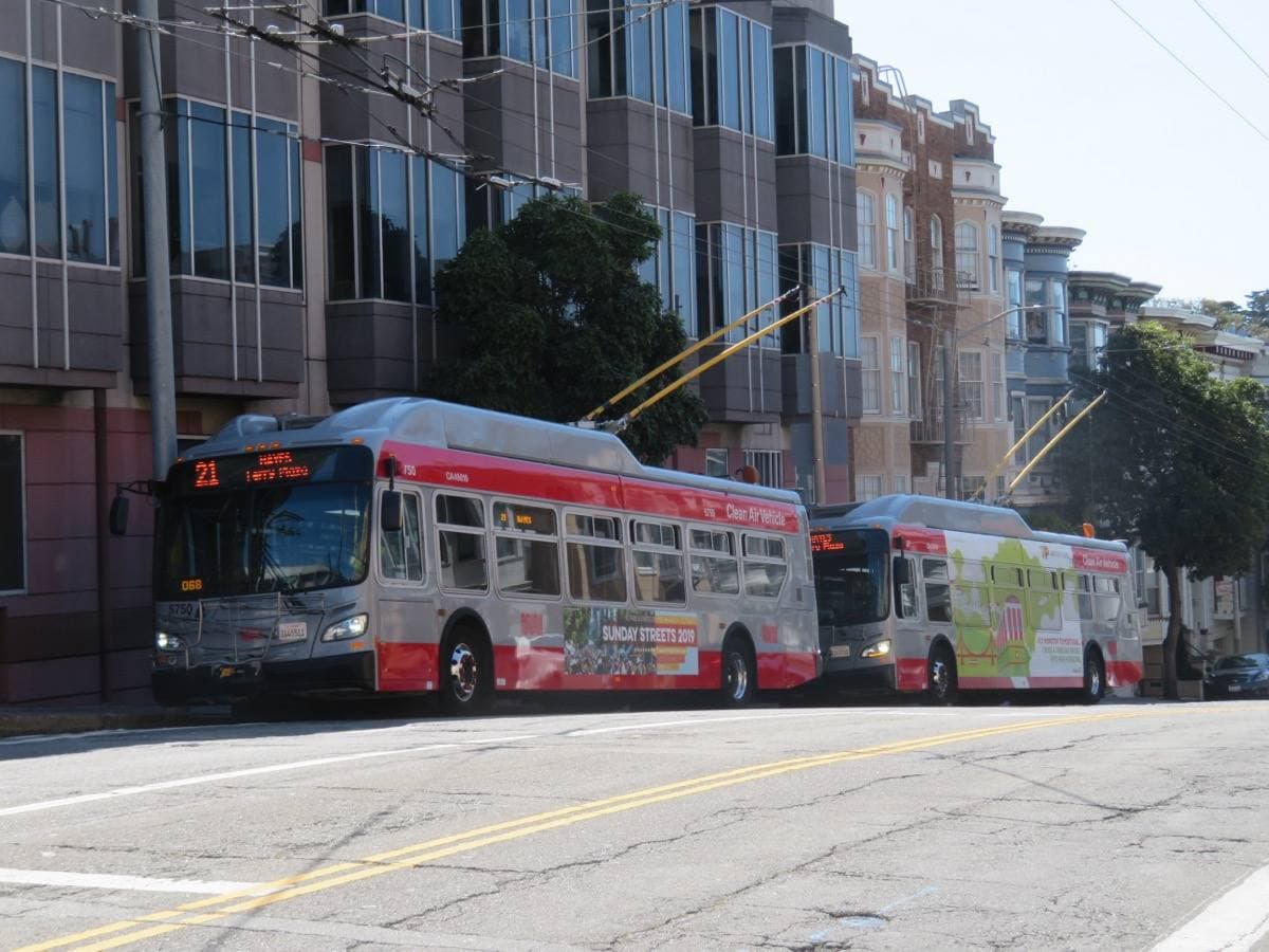 Two trolleybuses parked on Fulton Street in front of apartment buildings