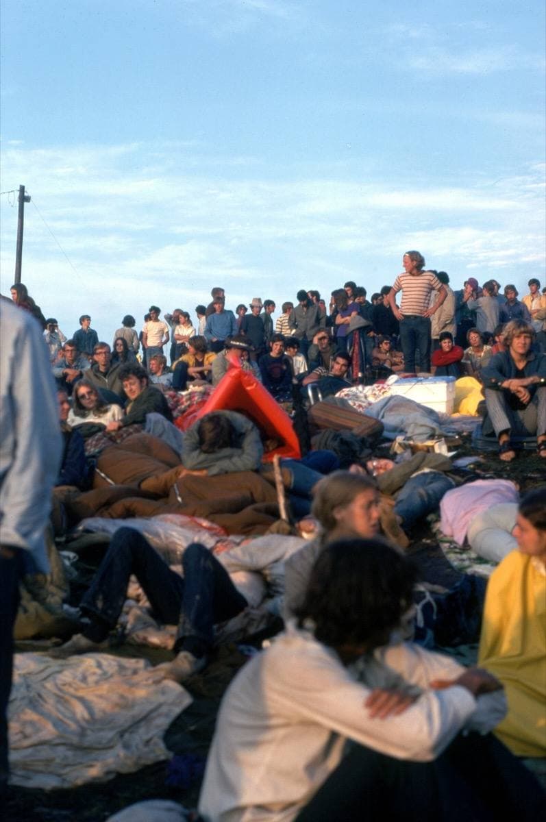 Festival-goers wrapped in blankets on a hillside in early morning light