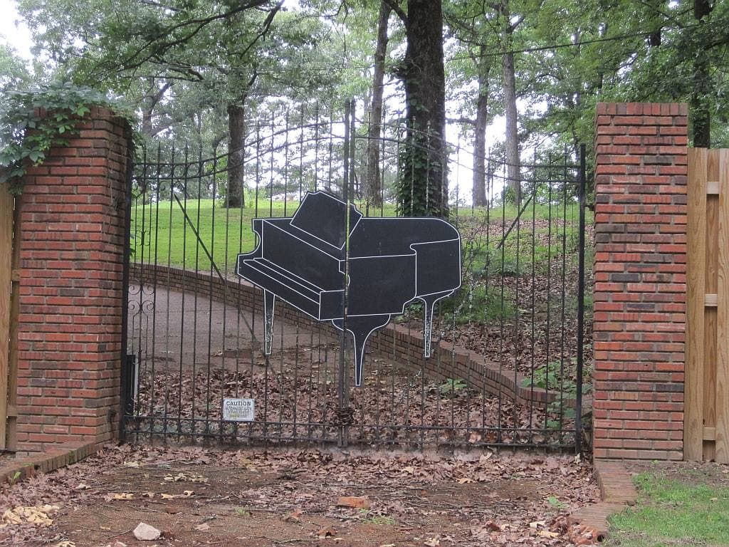 An iron gate between brick pillars with a black grand piano cut-out in it