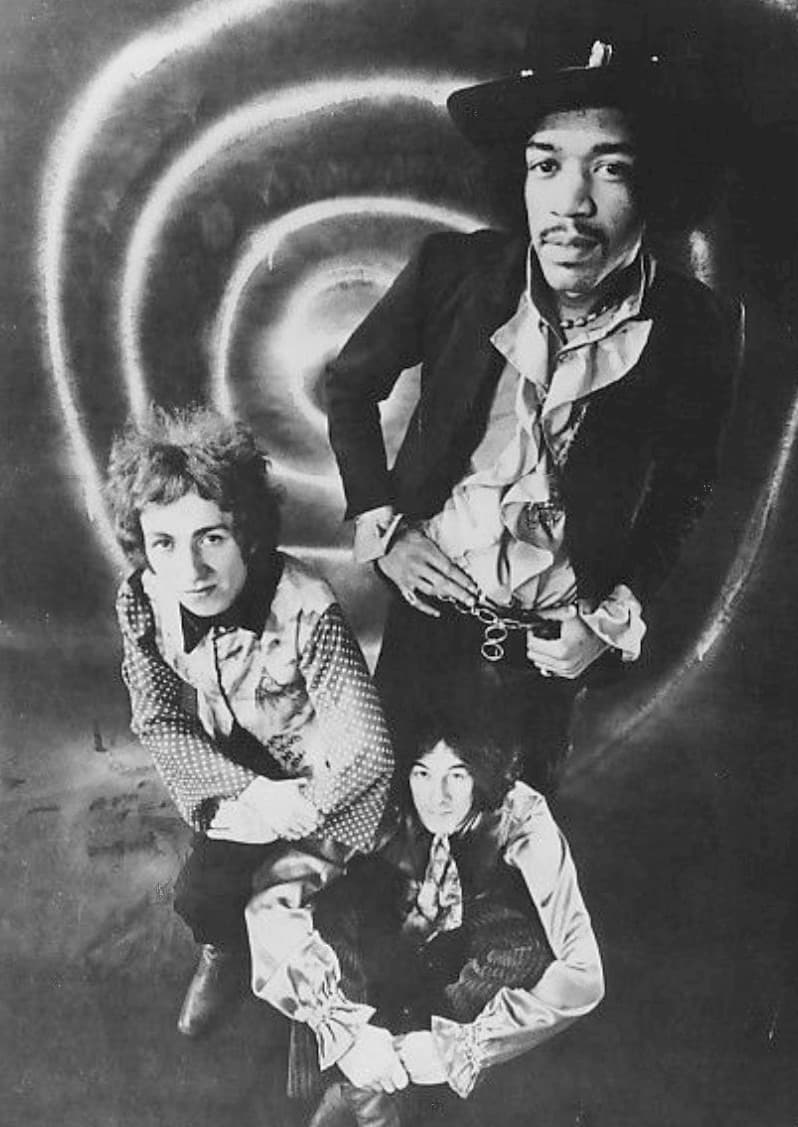 The three members of the Jimi Hendrix Experience posed in front of a swirling backdrop