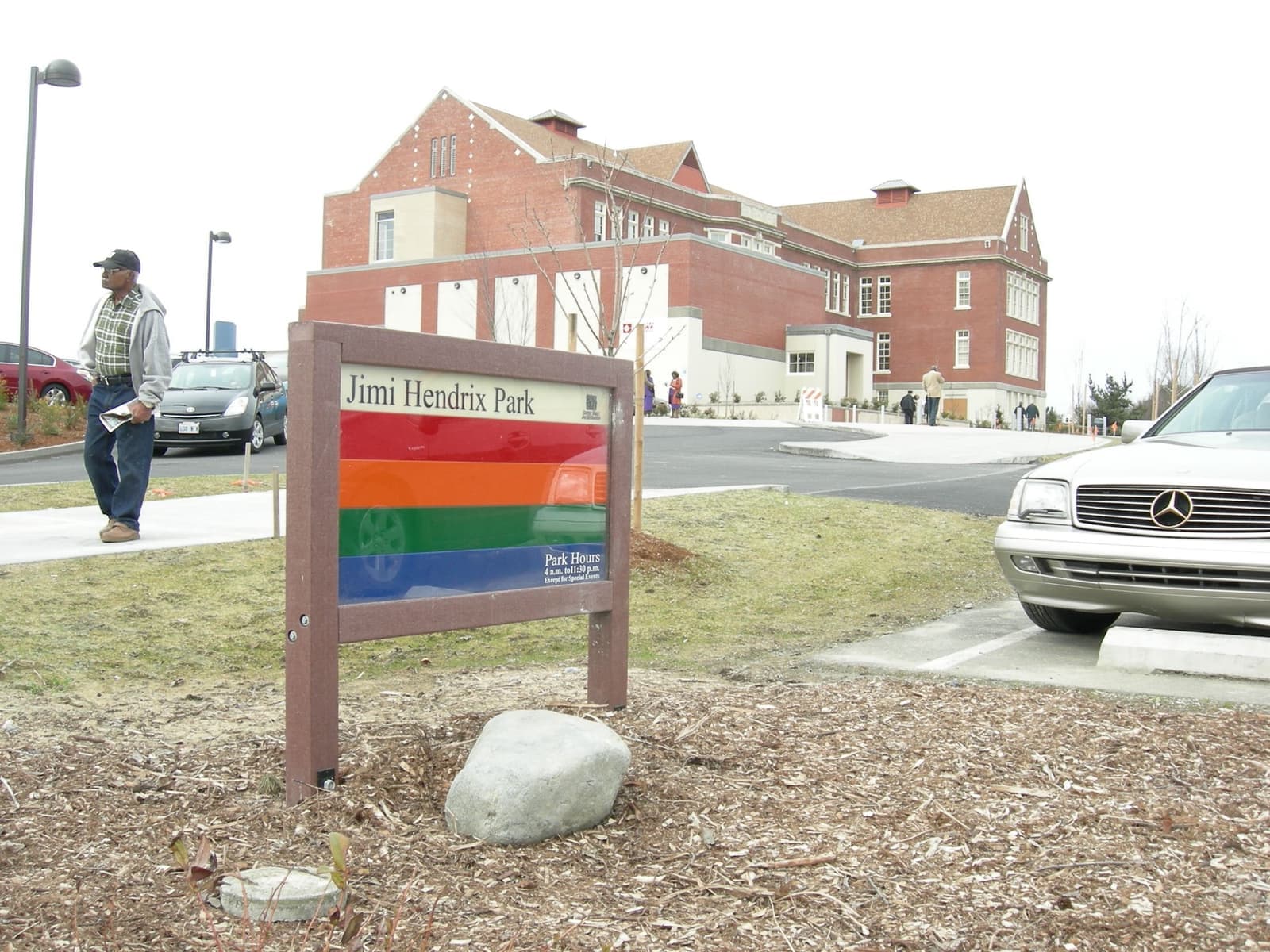 A rainbow-striped park sign in front of a brick school building