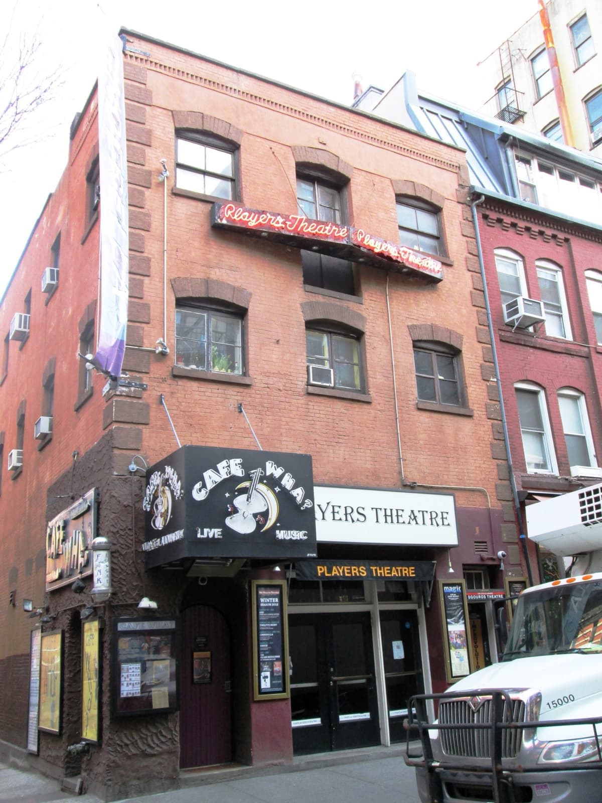 A brick building with the Cafe Wha? sign over a basement door