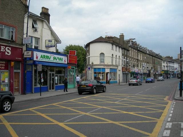 A busy south London high road with shops, terraced houses and a yellow box junction