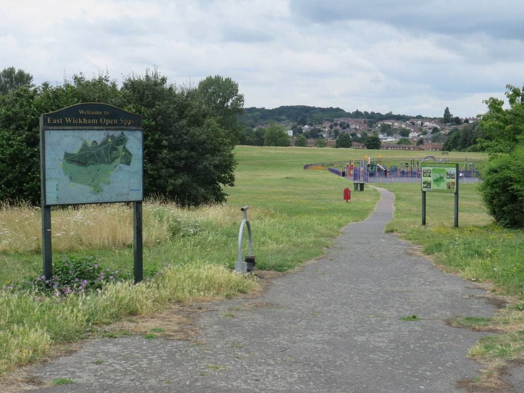 A grassy open space with a path and an information board, houses on the rise beyond