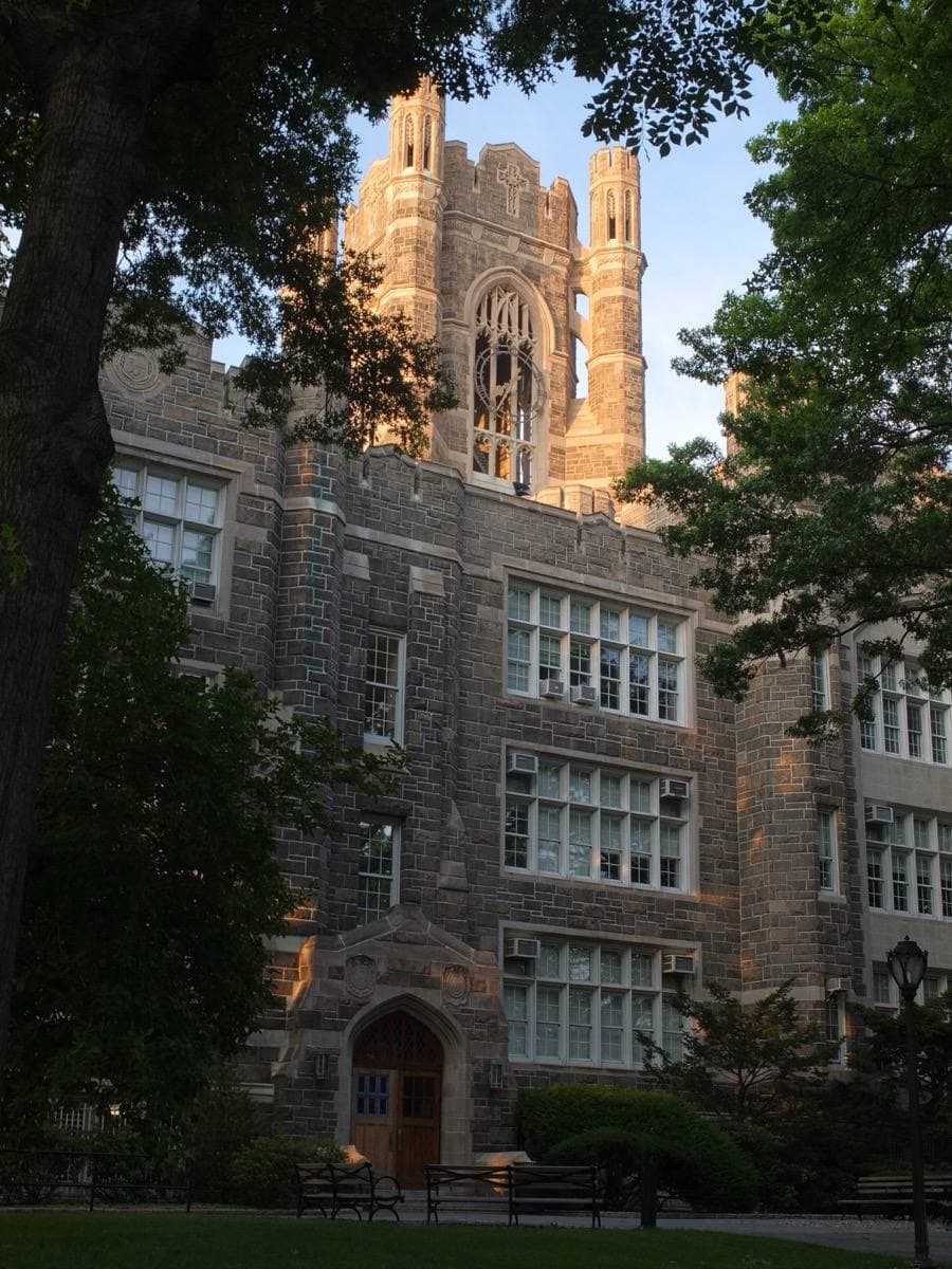 A Gothic stone hall with a tall tower behind a lawn