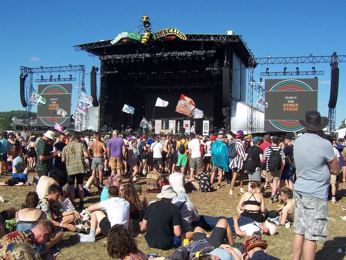 A big festival stage under a white canopy with a crowd in front