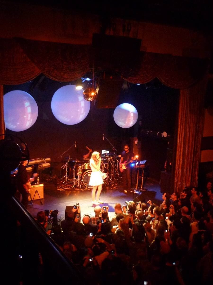 Lana Del Rey singing into a microphone under warm stage light