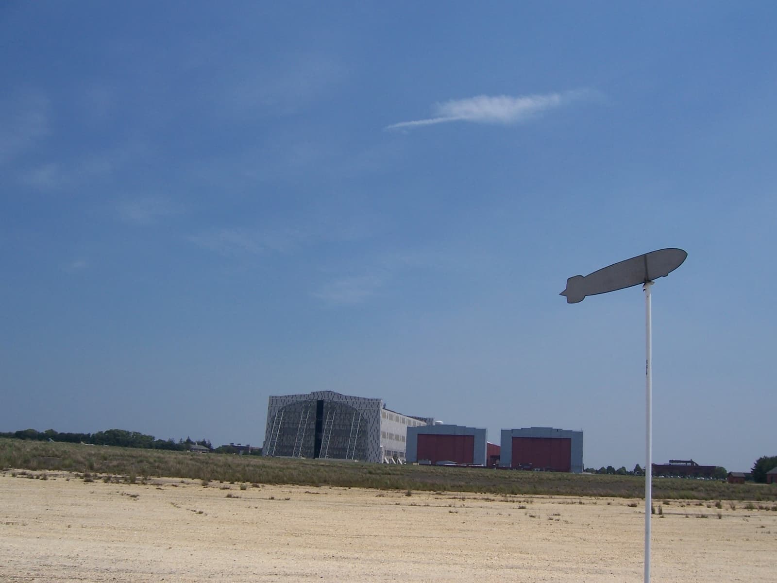 A low outline marker on grass marking where the Hindenburg came down, a hangar in the distance