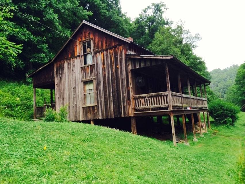 A small weathered wooden cabin with a porch among green trees