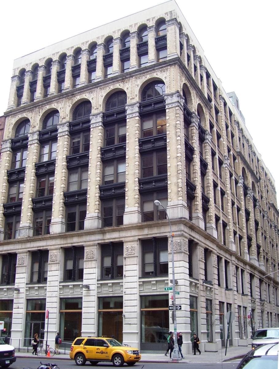 A tall pale stone 1900 building with arched upper windows on a Manhattan street corner