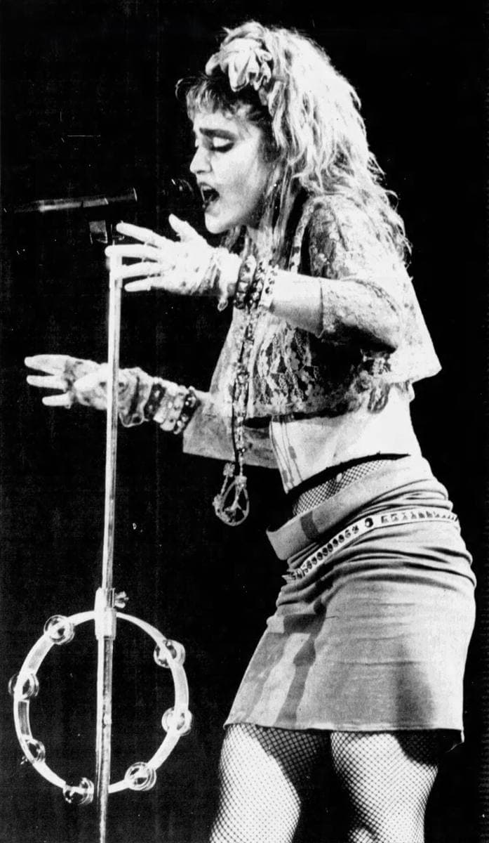 Madonna in lace, bangles and a short skirt singing at a microphone stand, black and white newspaper photograph