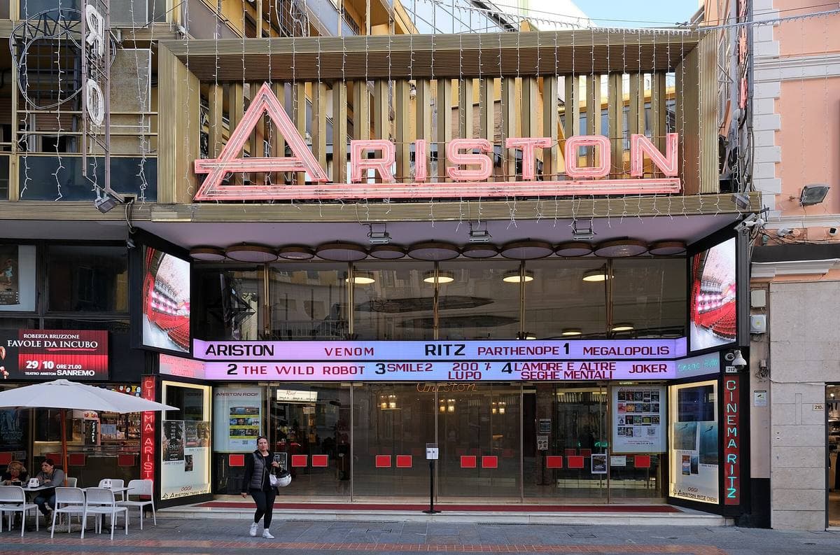 A cinema-theatre front with ARISTON in big pink letters above a lit canopy