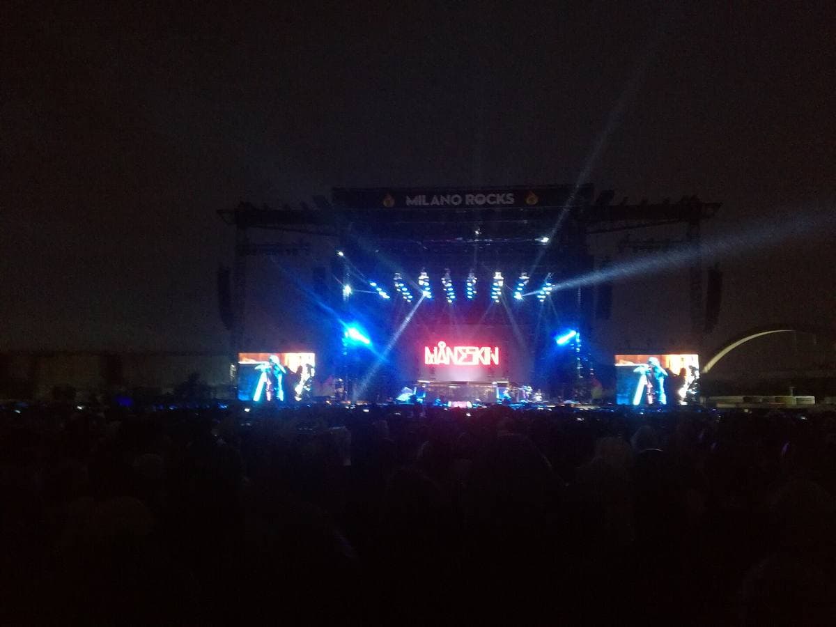 A festival stage at night, the band’s name in red on the screens, a dark crowd in front