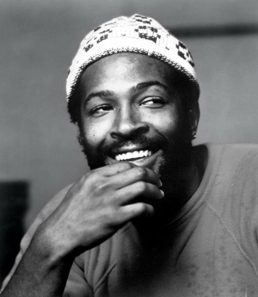 Marvin Gaye laughing, hand to his chin, in a patterned knitted cap and a sweatshirt