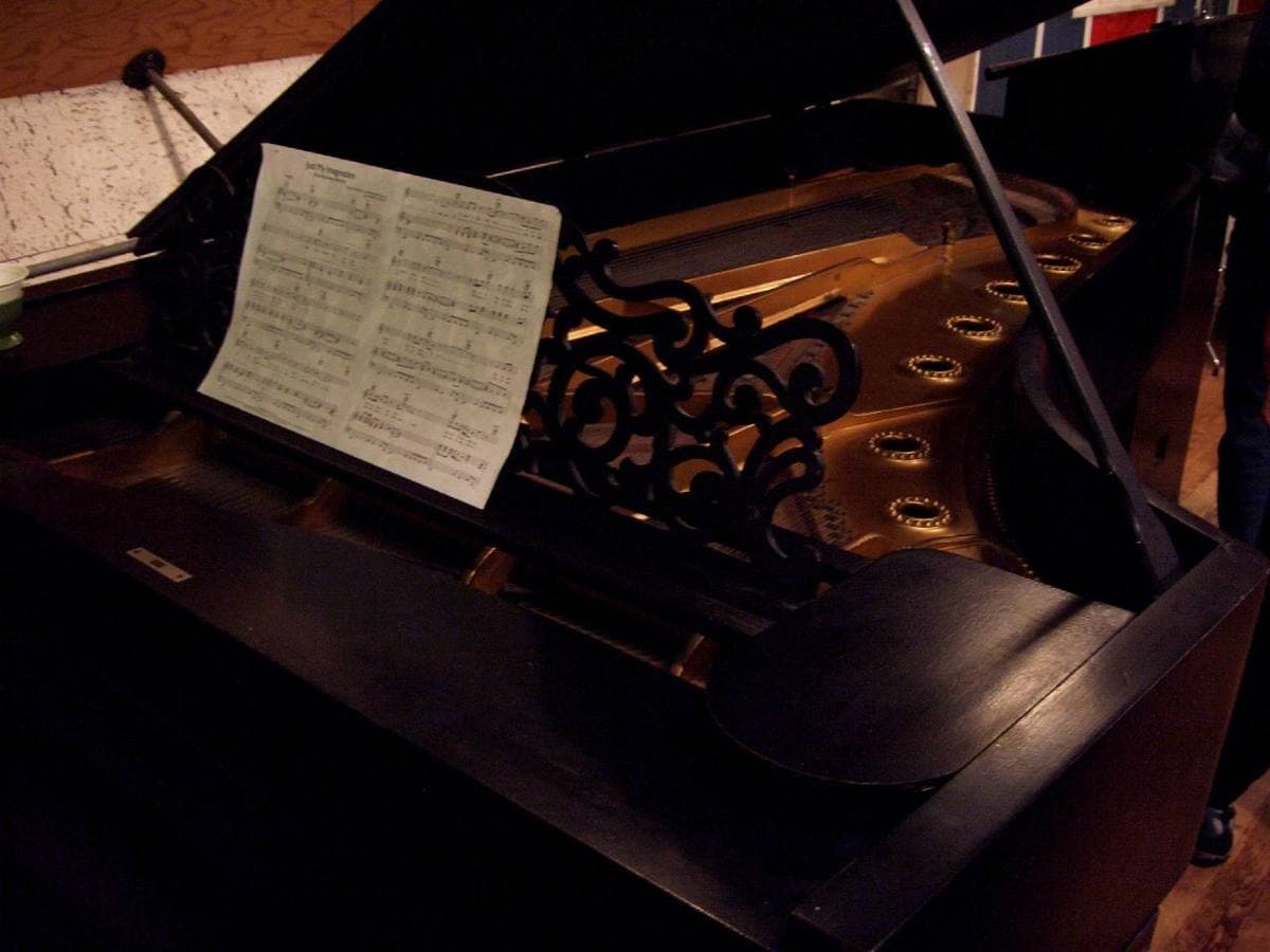 A dark grand piano with sheet music on its stand, in a dim studio