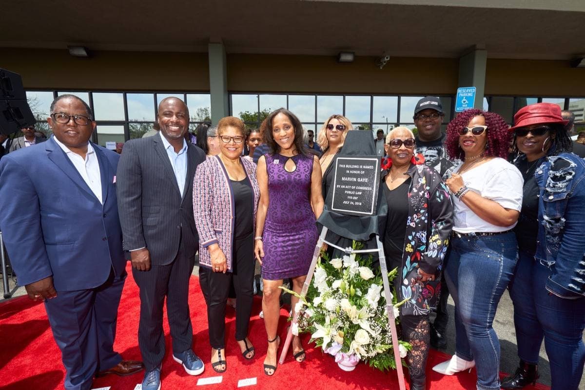 A group on a red carpet outside a post office, beside a plaque on an easel naming the building for Marvin Gaye