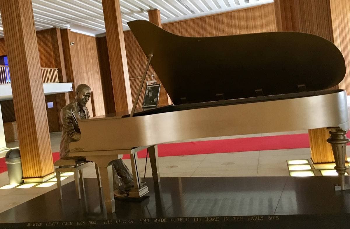 A bronze figure of Marvin Gaye seated at a gold grand piano in a wood-panelled hall