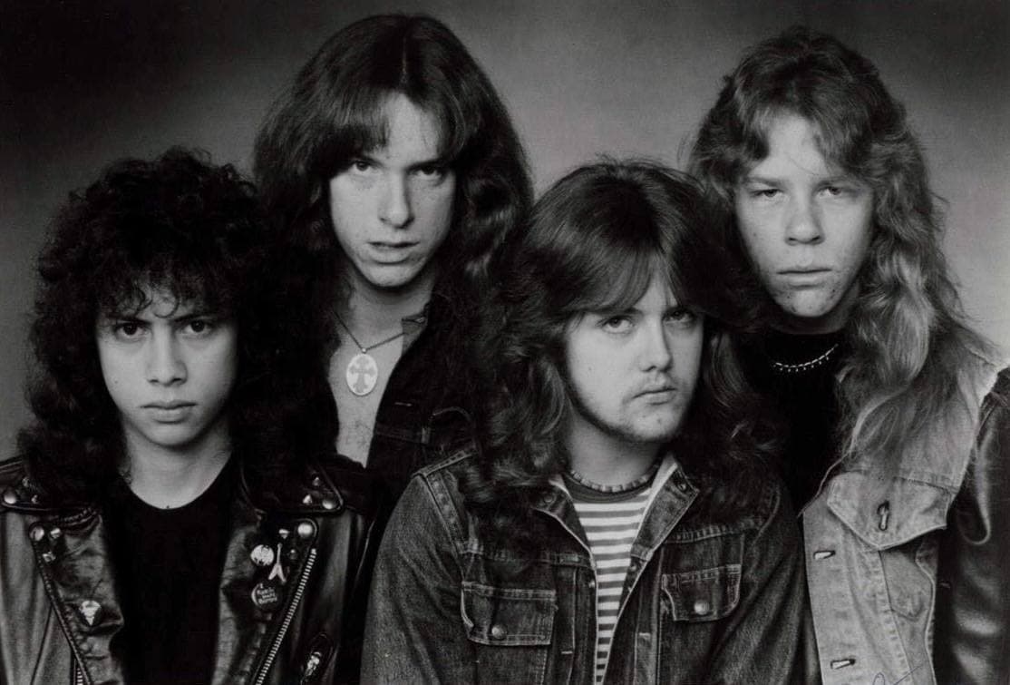 The four members of Metallica in 1983 in black and white: long hair, denim and leather jackets, unsmiling
