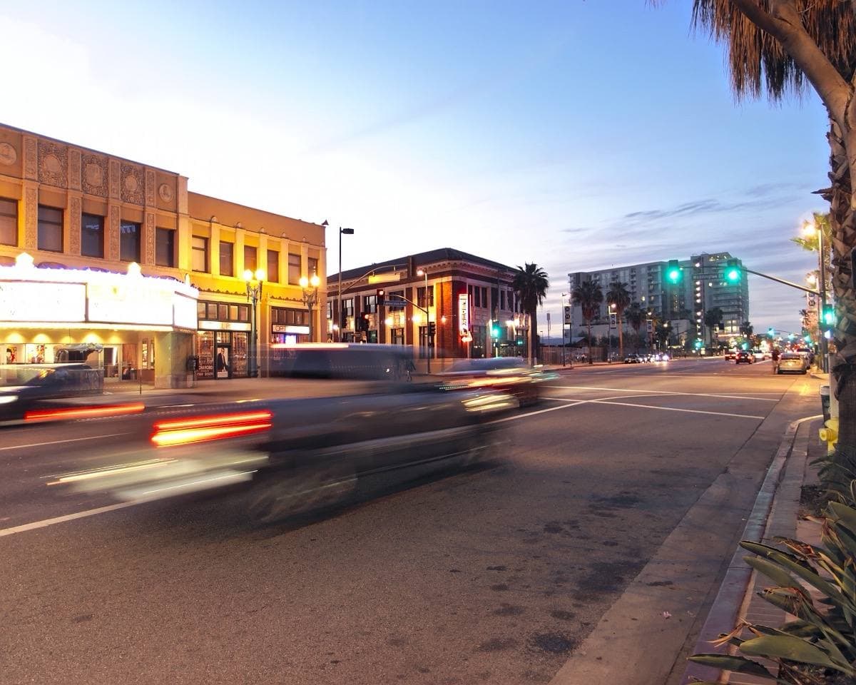 A North Hollywood boulevard at dusk, shopfronts lit and traffic passing