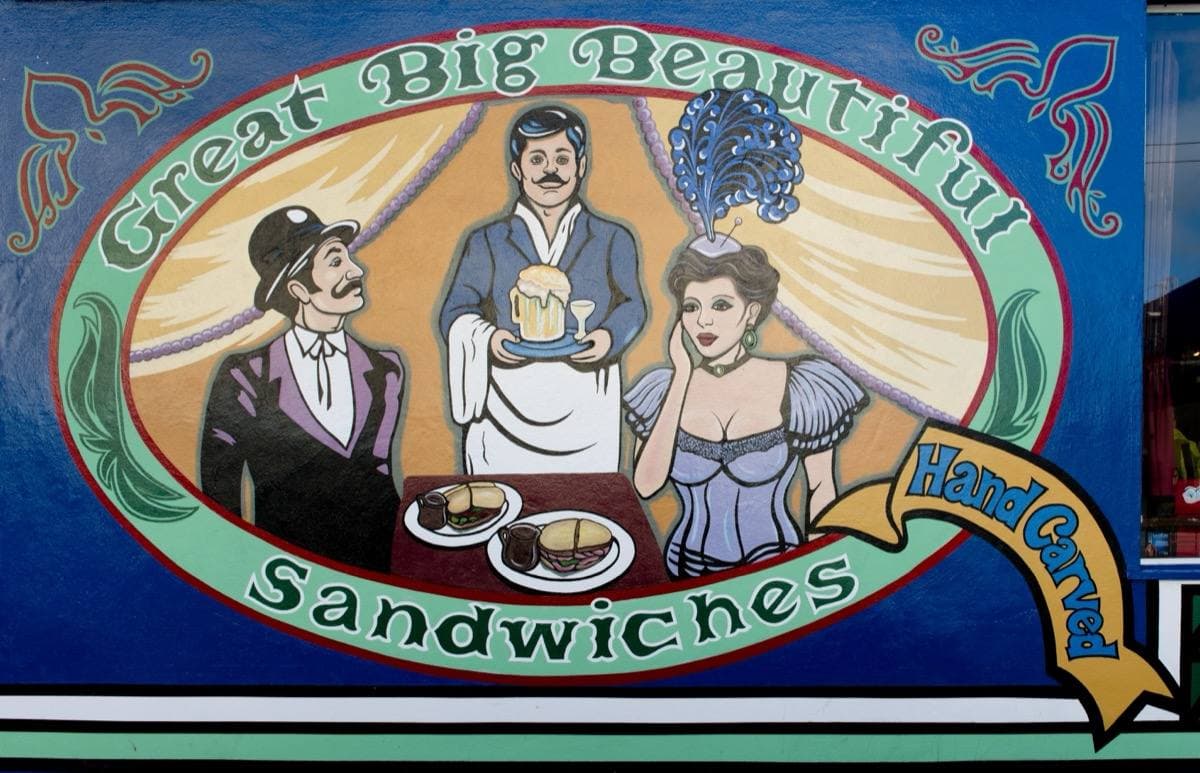 A corner restaurant painted with bright murals and lettering at a busy junction