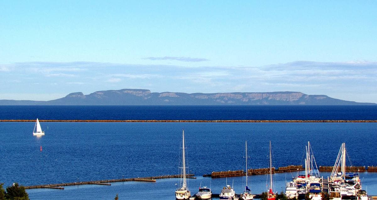 A long flat-topped headland on the horizon across blue water, sailing boats in a marina in front