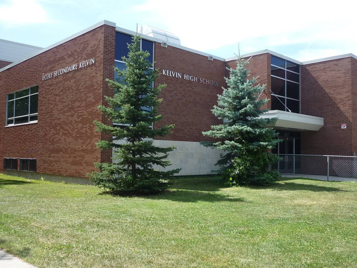 Brick and glass school building with evergreen trees on a lawn
