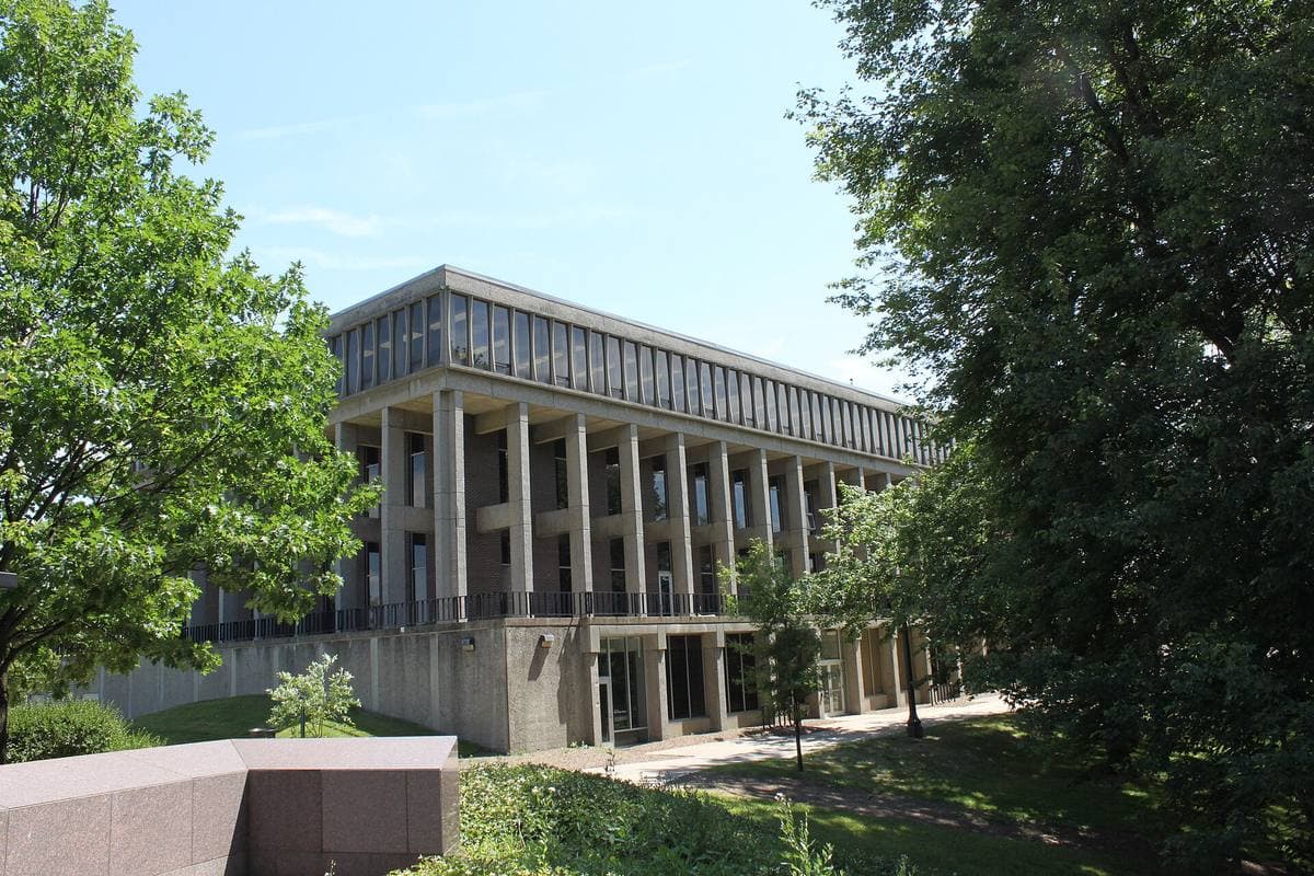 A modern building with tall square columns behind green trees