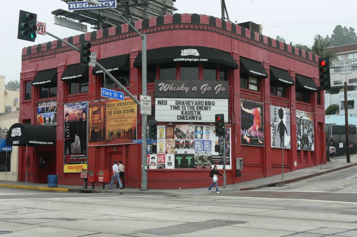Red corner club building with a marquee and posters on a sunny boulevard corner